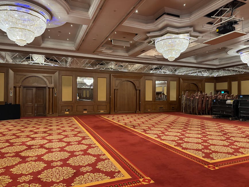 A modern indoor space featuring a long, grey upholstered furniture piece positioned centrally against a backdrop of red brick pillars. The flooring is wooden, and there are decorative plants in white 